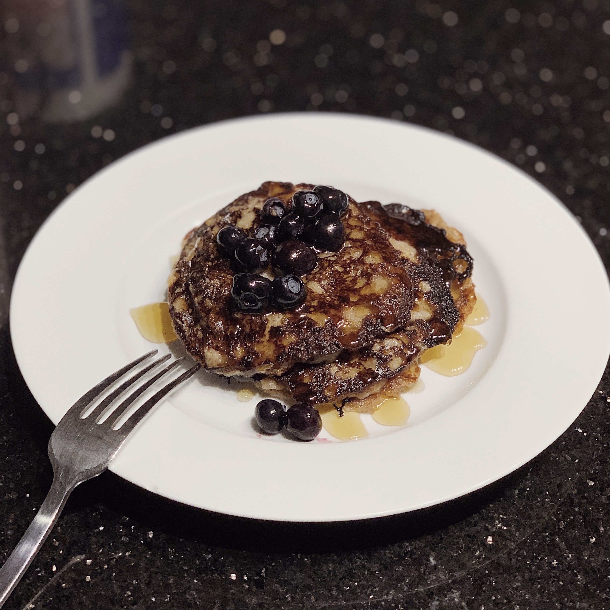 a photo of a stack of banana-based pancakes with honey and blueberries on top