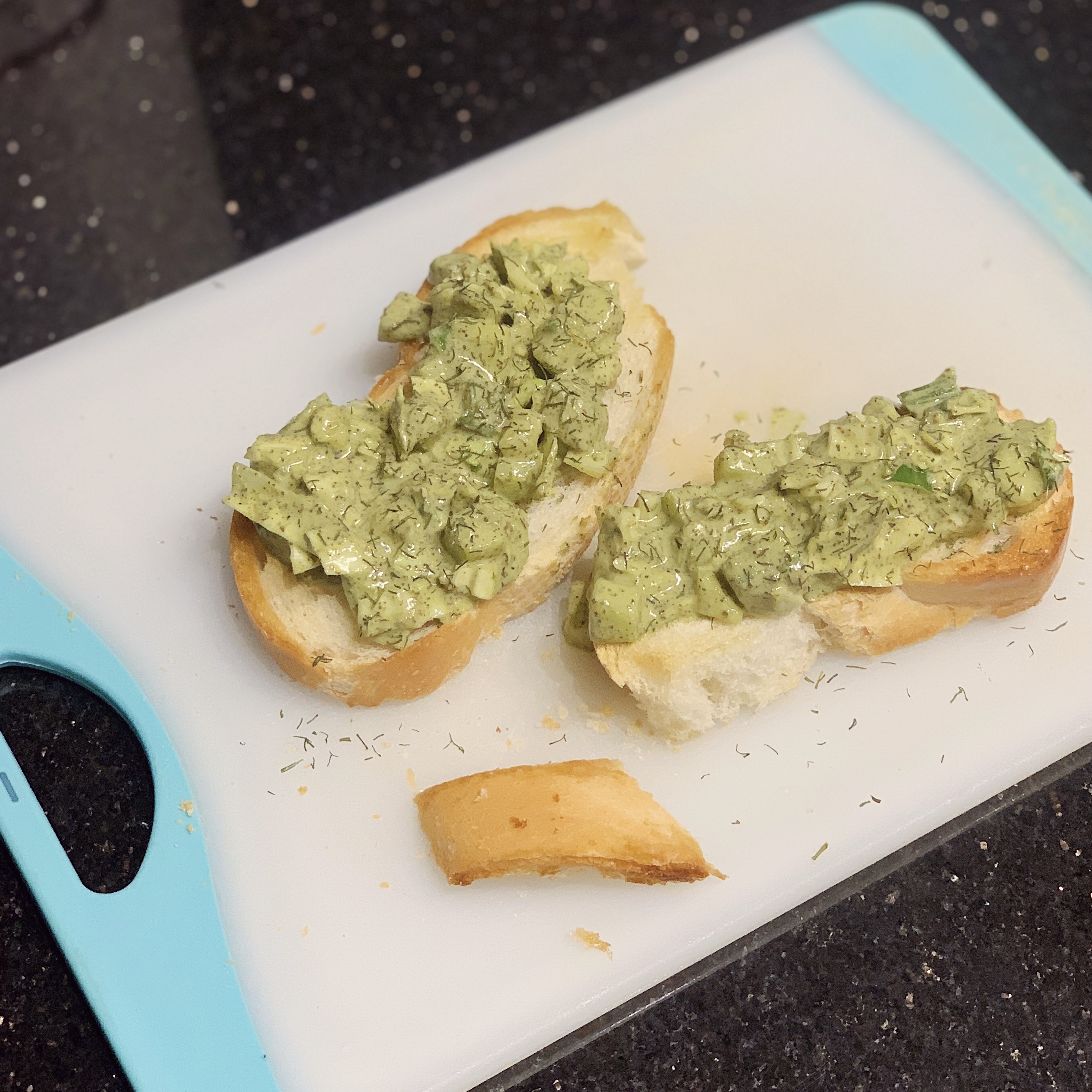 a cutting board with two slices of bread with green goddess dip